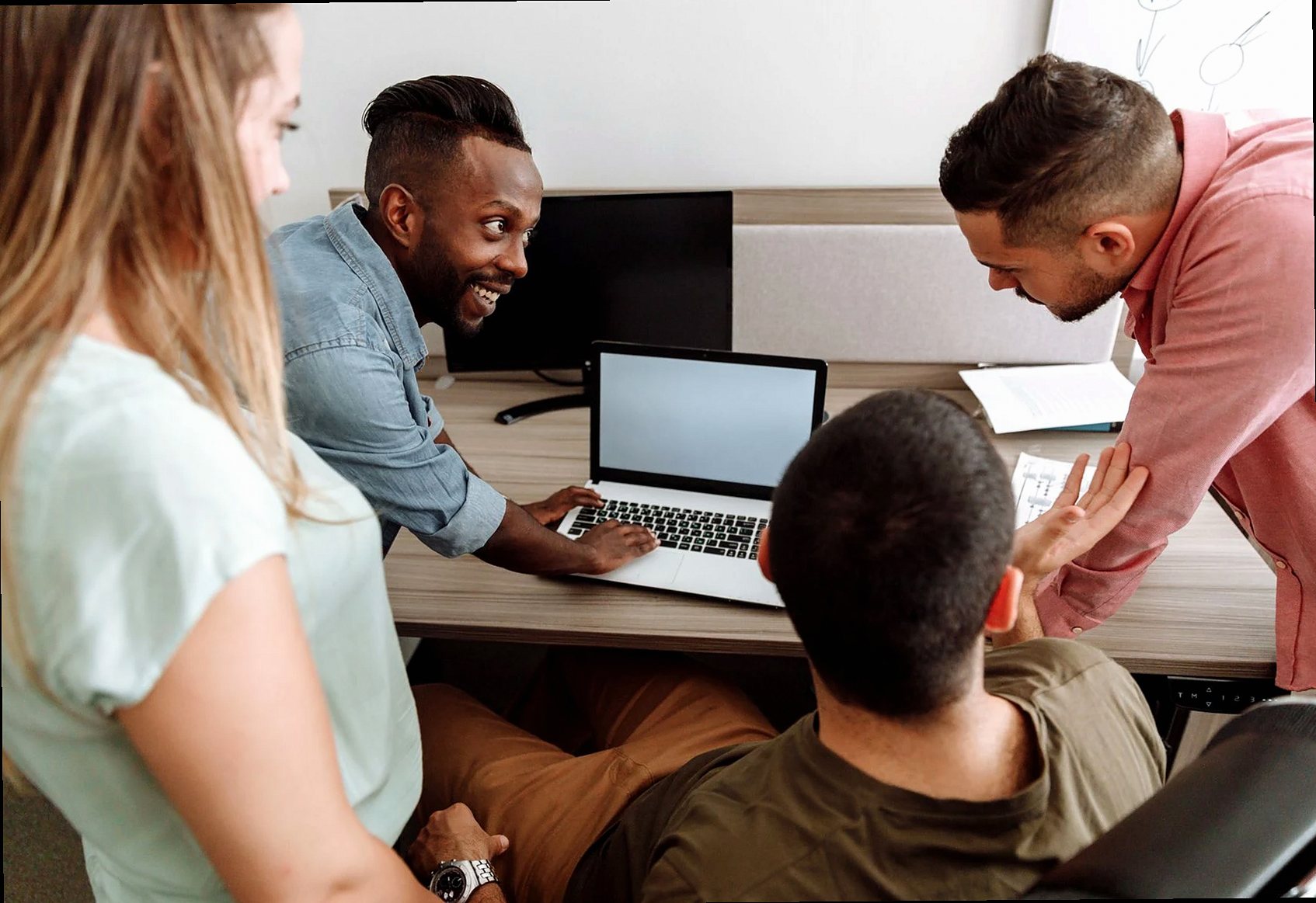 Four colleagues brainstorming around a laptop in a bright, modern office setting.